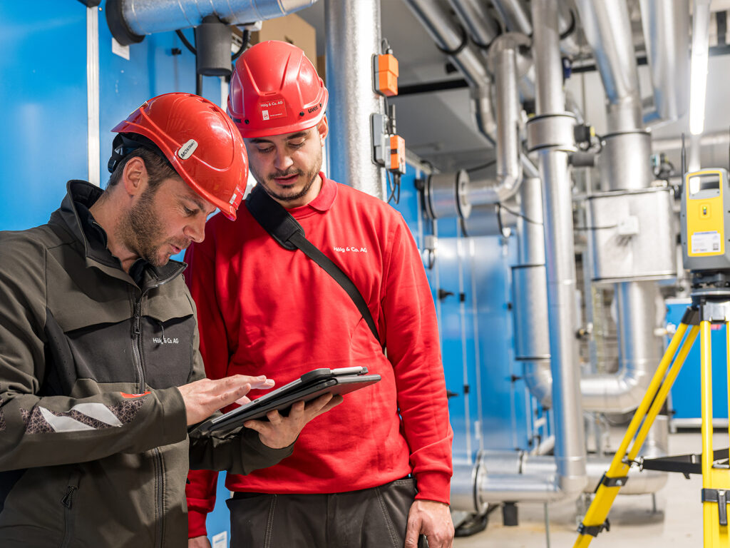 Zwei Mitarbeitende der Hälg Group blicken auf ein Tablet mit dem digitalen Plan der Baustelle.