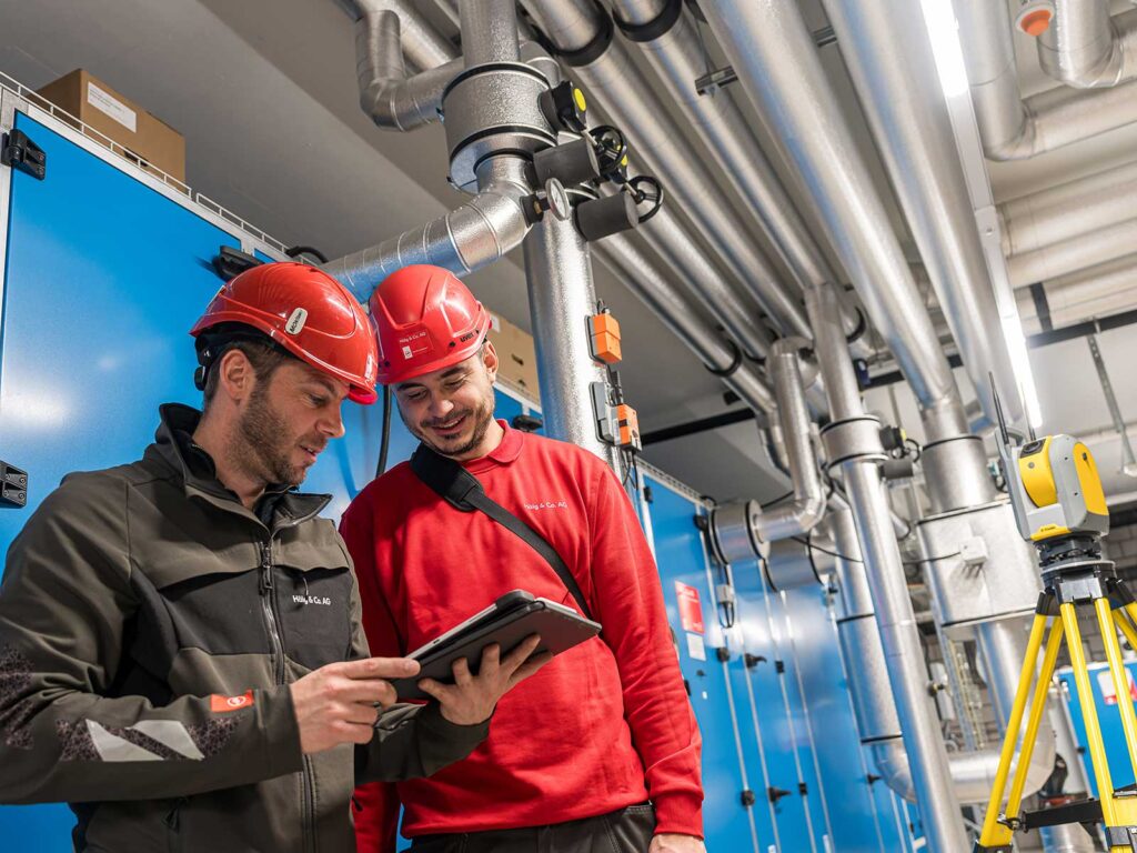 Zwei Mitarbeitende der Hälg Group blicken auf ein Tablet mit dem digitalen Plan der Baustelle.