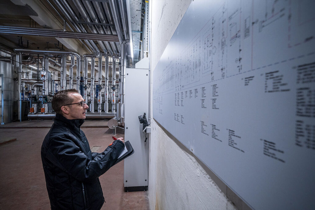 Projektleiter der Hälg Group steht in riesigem Technikraum vor einem Plan.