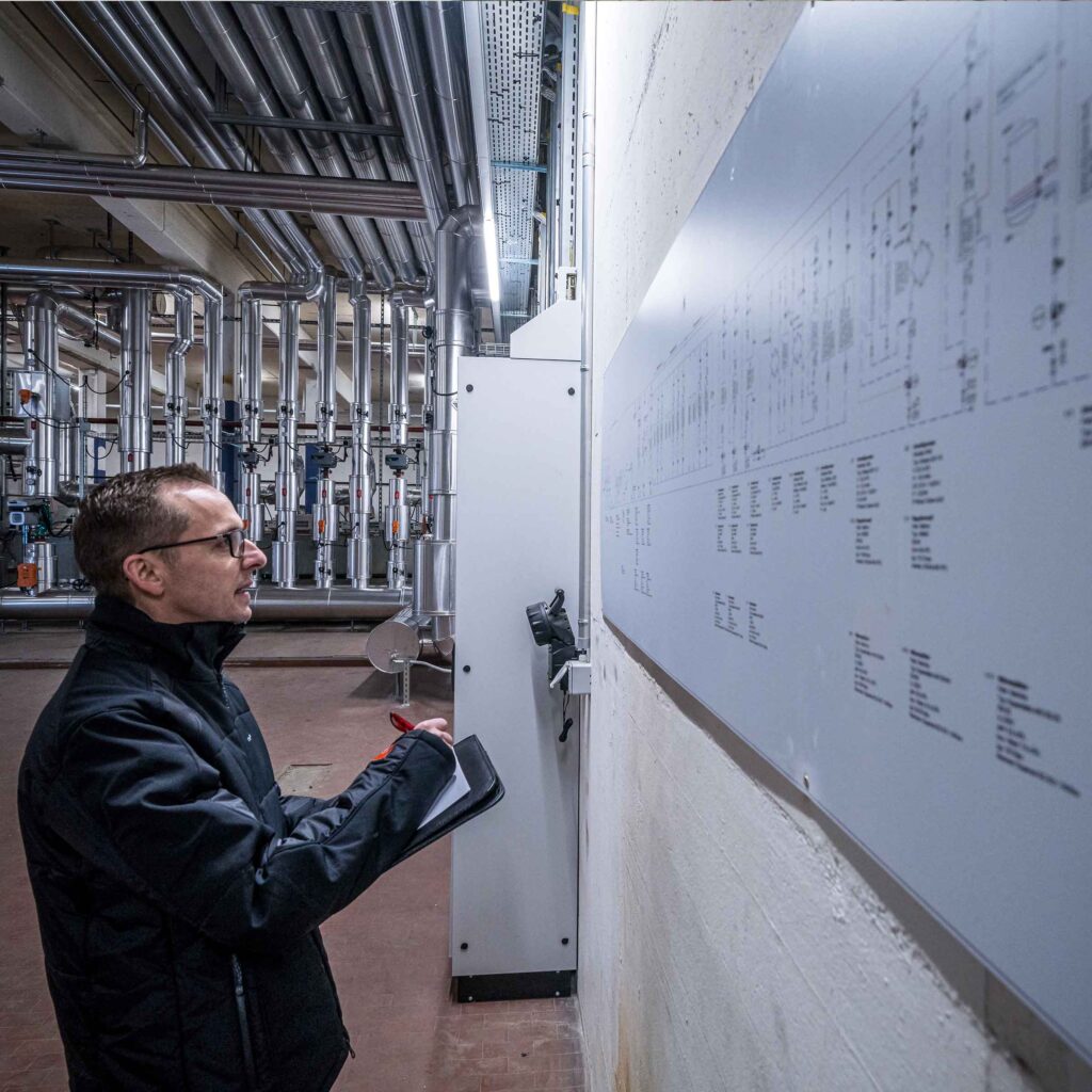 Projektleiter steht in Technikzentrale vor einem grossen Plan an der Wand.