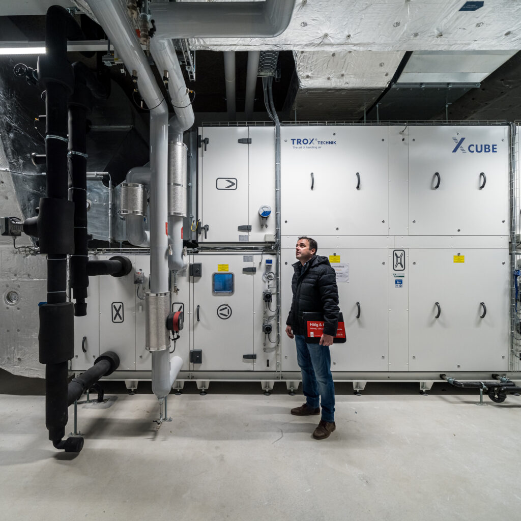 Un chef de projet de Hälg Group se trouve dans une centrale technique et regarde la nouvelle technique du bâtiment installée.