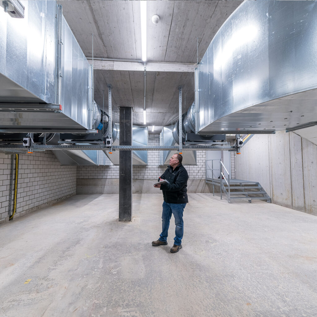 Un chef de projet Ventilation/Climatisation de Hälg & Cie SA à St-Gall se tient sous les gigantesques installations de ventilation de la halle SGKB à St-Gall.