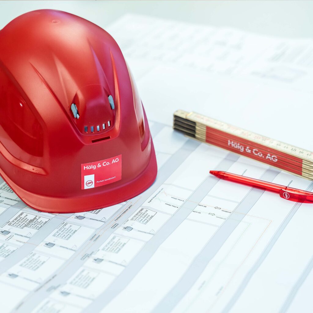 Un casque, un mètre pliant et un crayon sont posés sur un plan de construction.