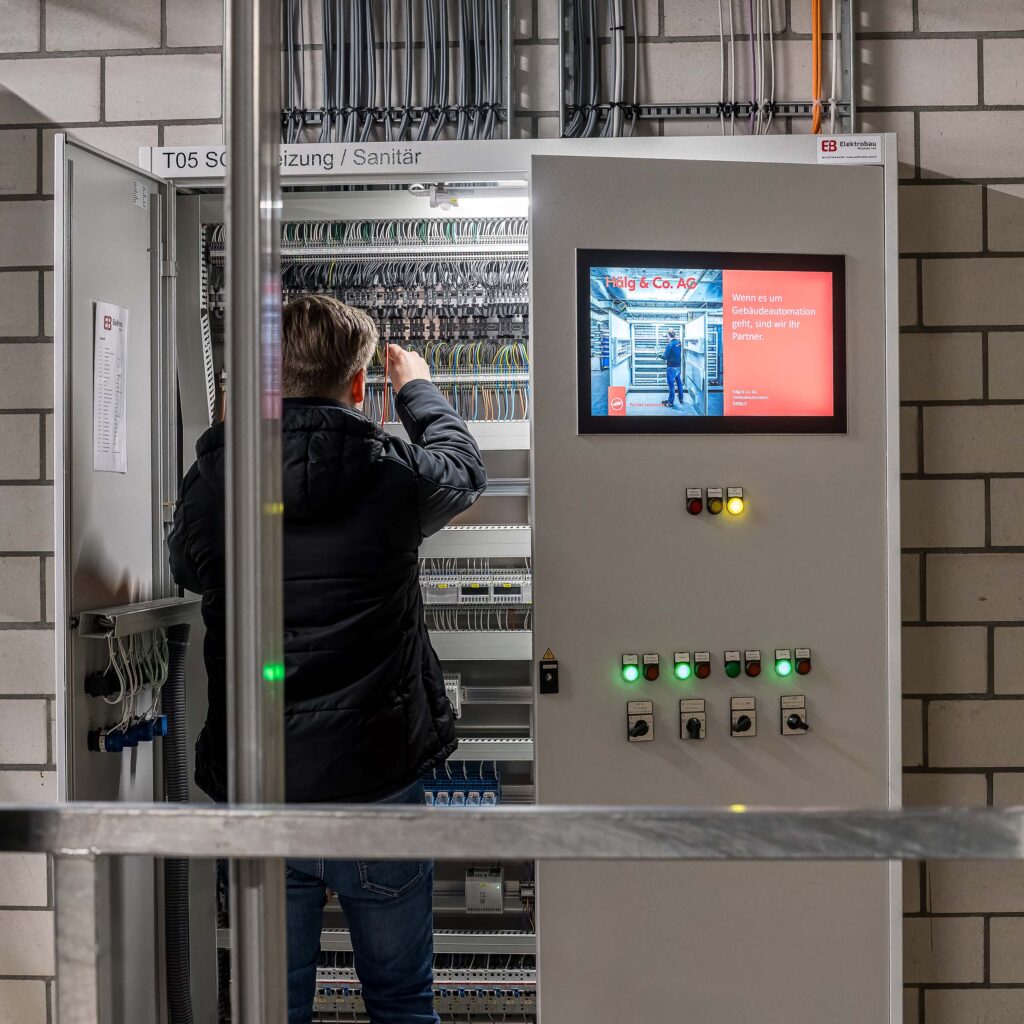 Un collaborateur de Hälg & Cie SA Automatisation de bâtiment se tient devant l'armoire électrique pour les installations CVCS de la halle SGKB à St-Gall.