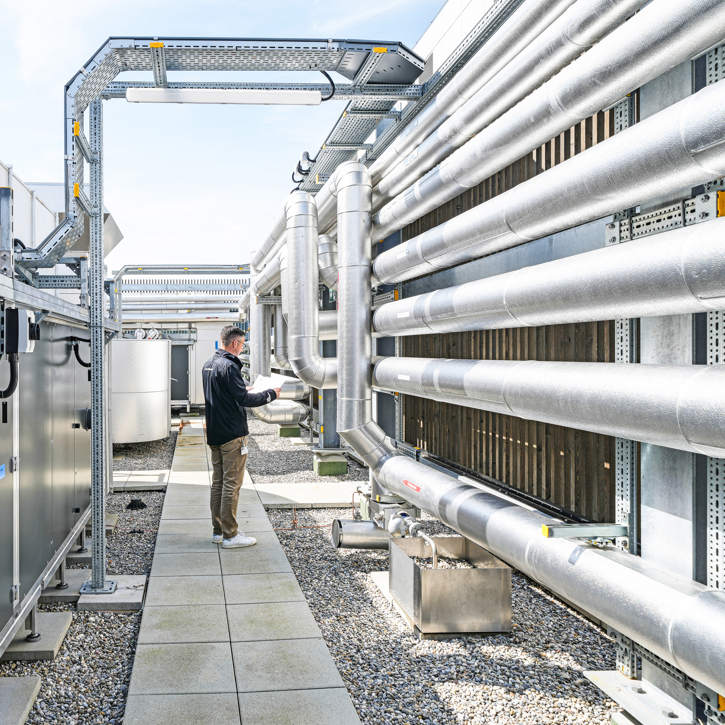 Projektleiter der Klima AG in Basel steht vor einer Lüftungsanlage mit einem Plan in der Hand.