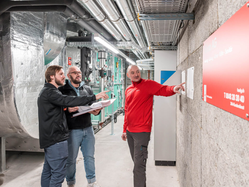 Drei Mitarbeitende der Klima AG Basel in der Lüftungszentrale von Transa Basel.