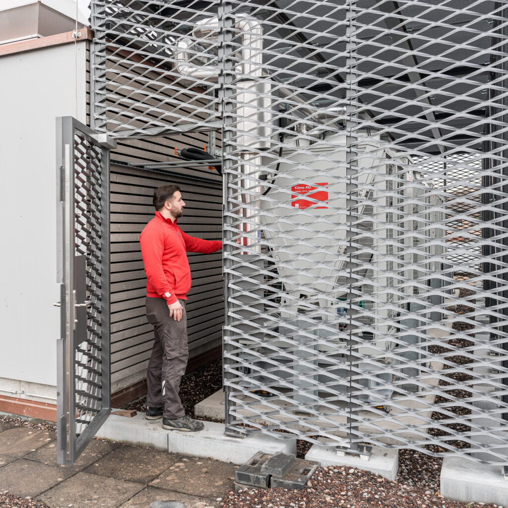 Ein Installateur der Klima AG Basel steht vor eine gebäudetechnischen Anlage.