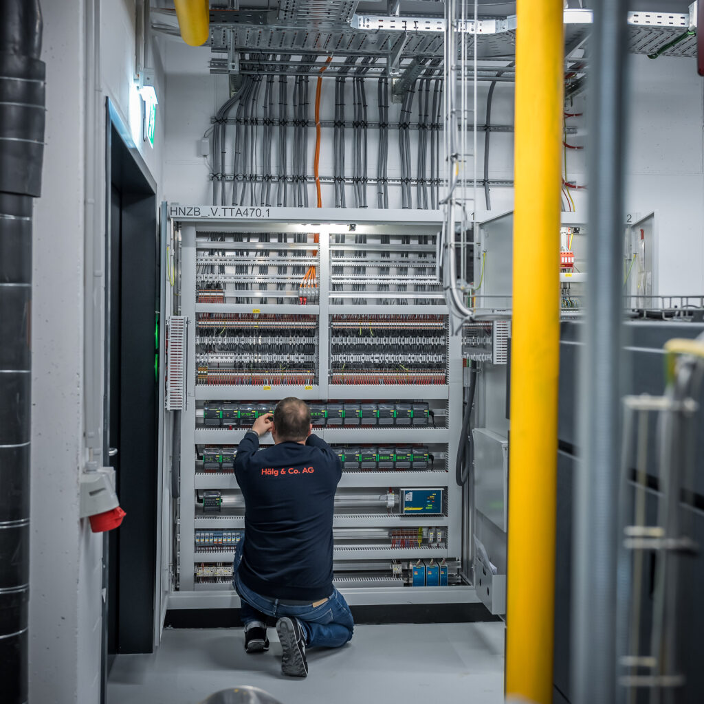 Projektleiter Gebäudeautomation der Hälg & Co. AG vor einem Schaltschrank.