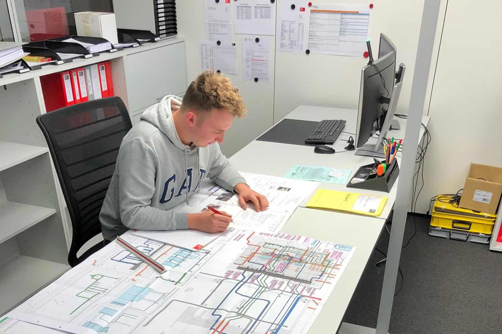 Gebäudetechnikplaner Lüftung in Ausbildung am Schreibtisch am Zeichnen eines Plans